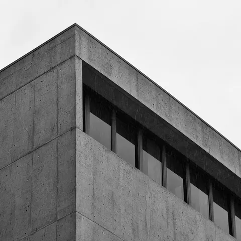 A monochrome upward crop of a concrete roof corner with recessed glazing and fine rain marks.