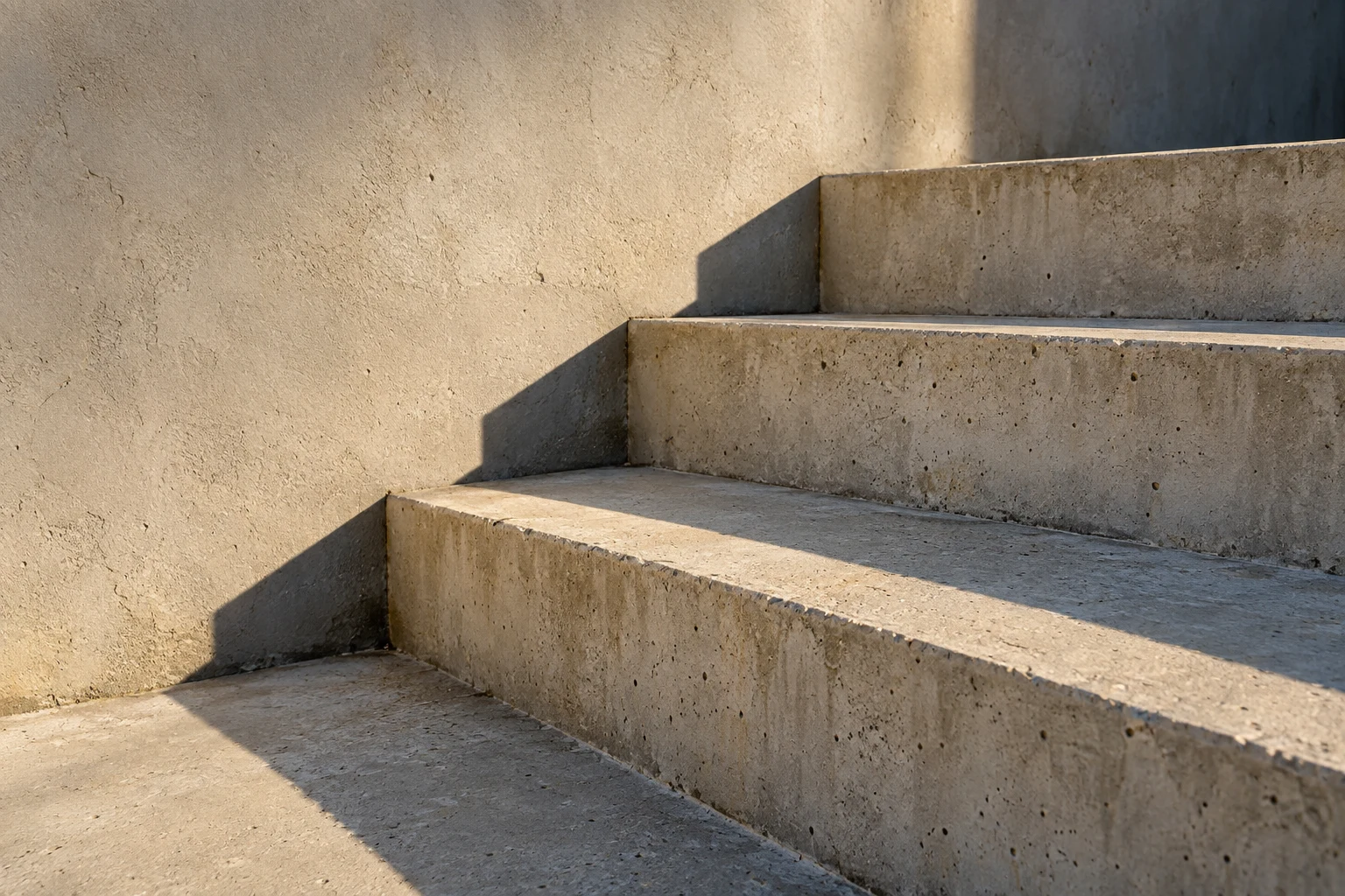 Three pale concrete steps with crisp diagonal shadows and fine worn surface detail.