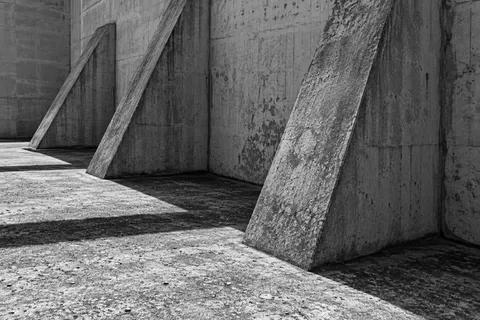 A monochrome close view of three sloping concrete buttresses and long shadows.