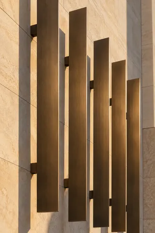 Five brushed bronze vertical fins mounted away from a pale wall in warm side light.