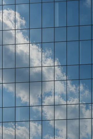 White cloud reflections crossing a close blue curtain wall with fine dark mullions.