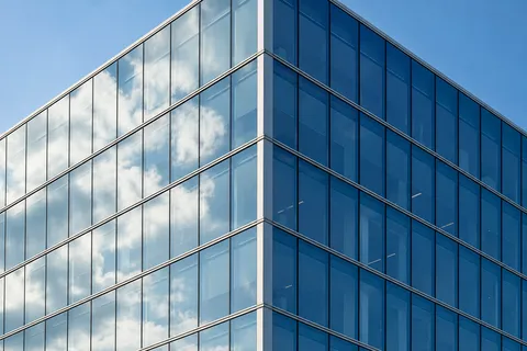Two faces of a modern glass building reflect pale clouds and darker blue sky around a silver corner trim.