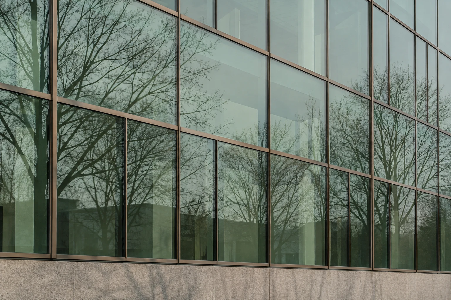 Leafless trees reflected across green-tinted office windows above a pale stone base.
