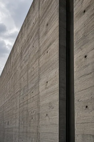 A close upward view of board-formed gray concrete, circular tie holes and a deep vertical gap.