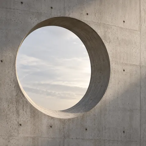A large round opening through textured pale concrete with a shaded inner reveal and soft sky beyond.