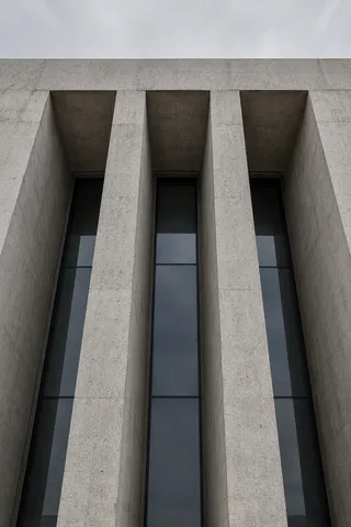 An upward view of three tall recessed window bays in a heavy pale concrete facade.