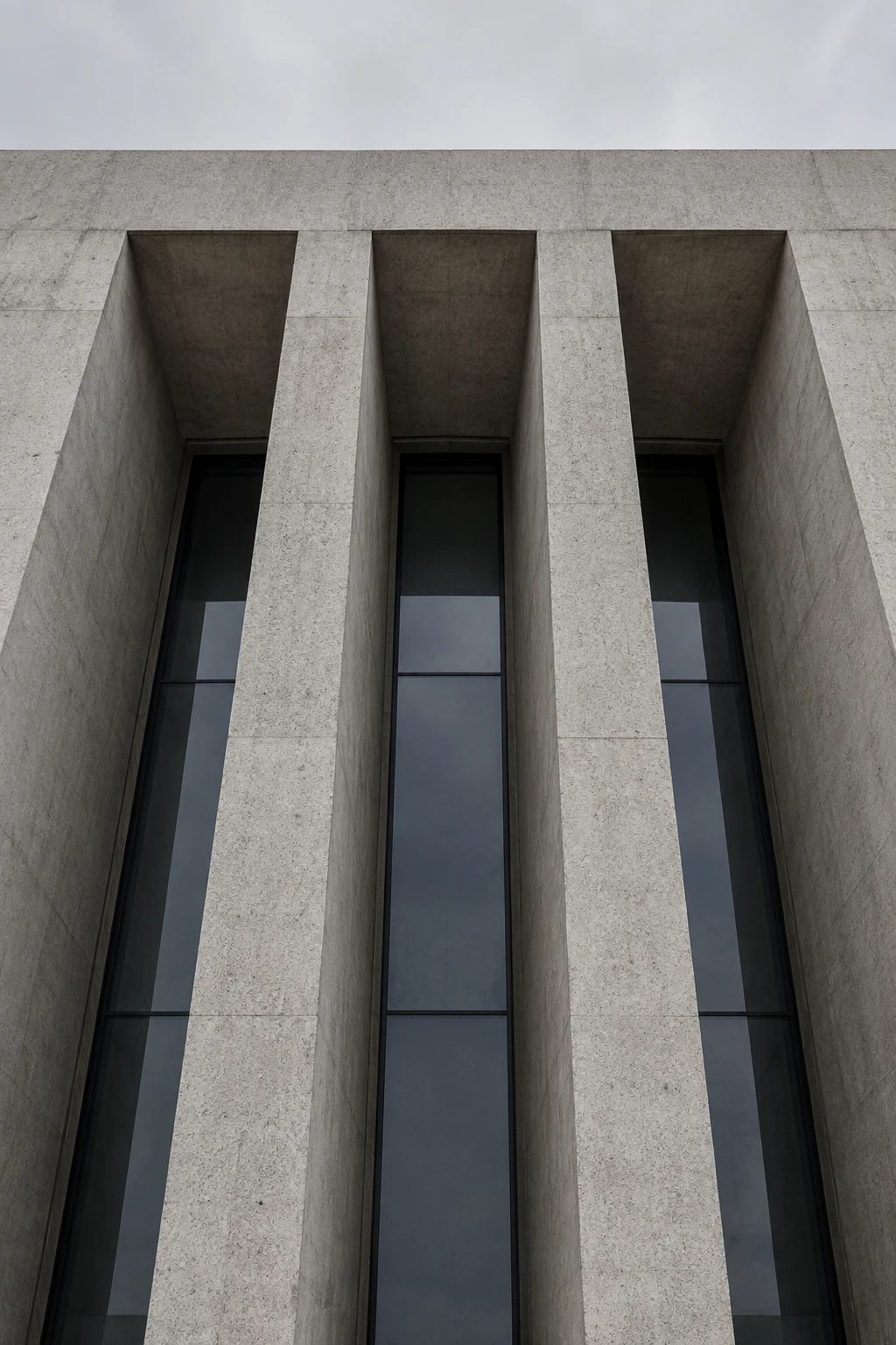An upward view of three tall recessed window bays in a heavy pale concrete facade.