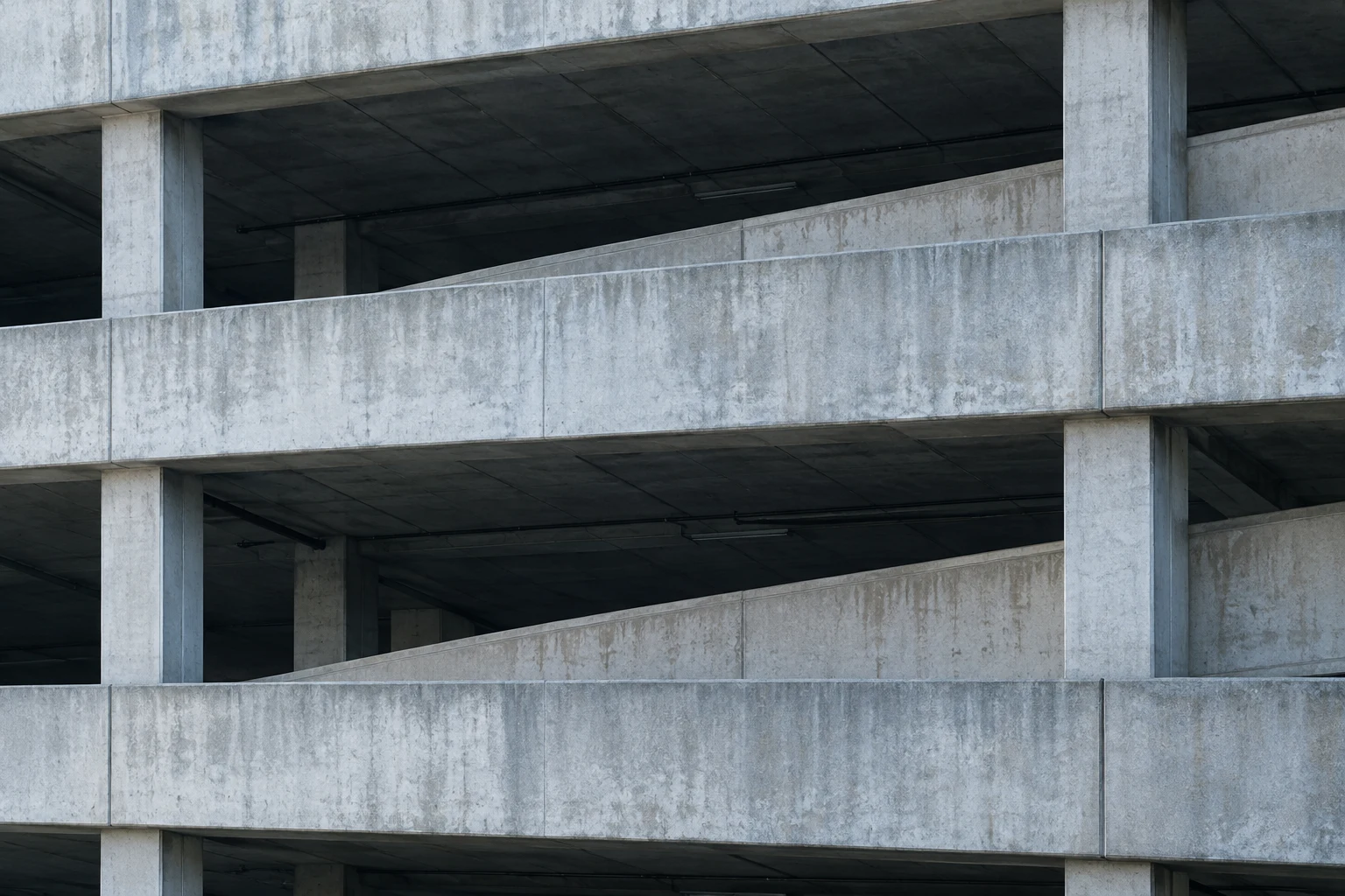 A close exterior view of an empty concrete parking structure with open bays and a diagonal ramp.