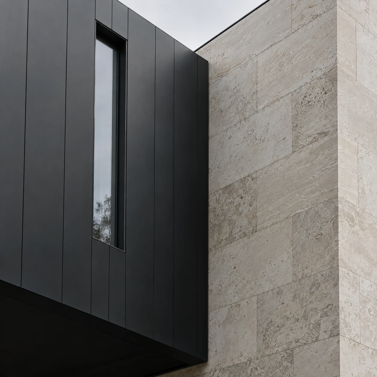 A charcoal metal facade with a slender window beside pale limestone blocks, seen at an upward angle.