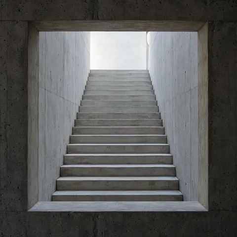 A pale straight staircase seen through a deep square opening in a darker concrete wall.