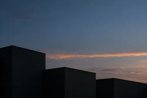 Three anonymous flat-roof buildings in shadow below a blue-gray evening sky and muted peach clouds.