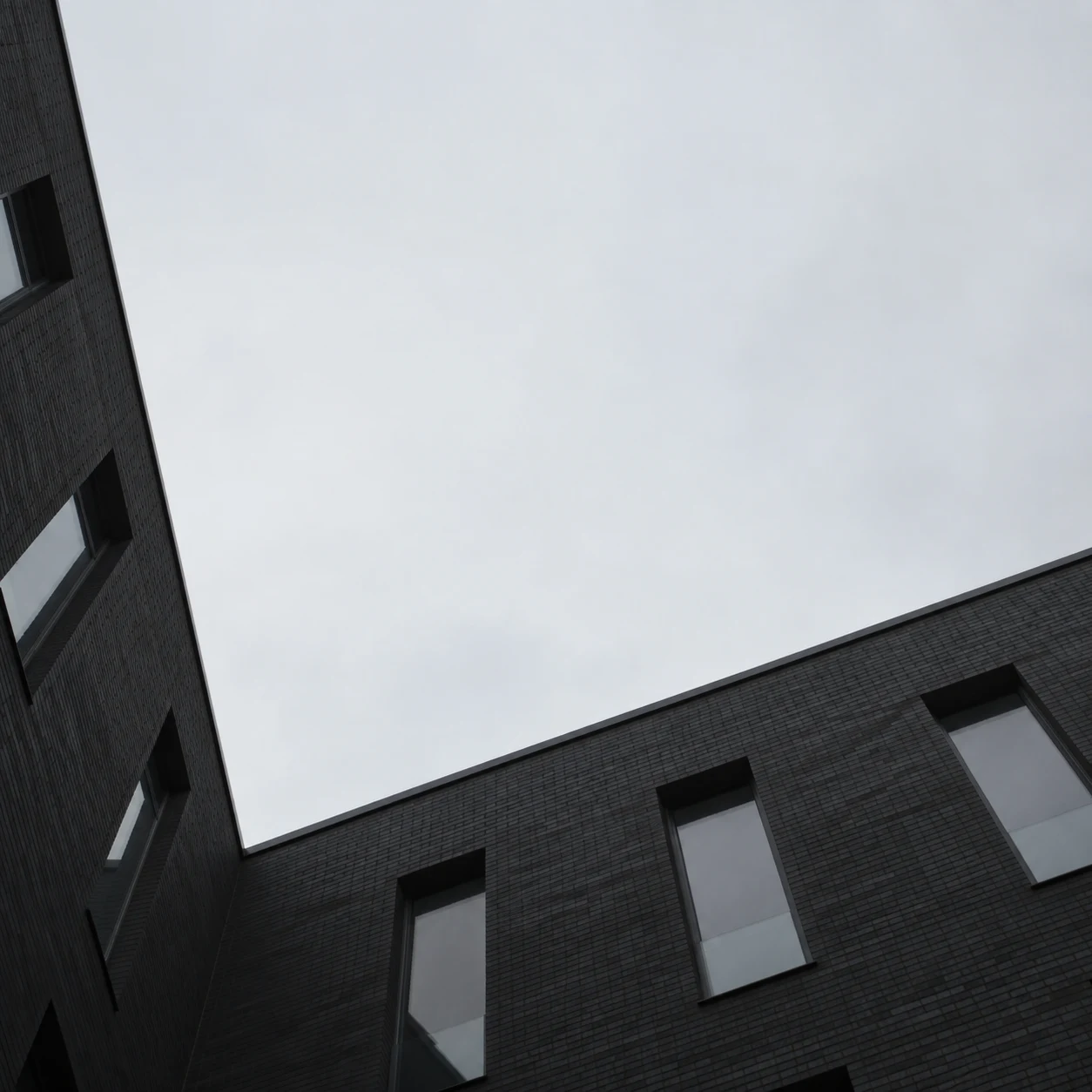 An upward courtyard view of two dark brick building wings around a large asymmetrical shape of gray sky.