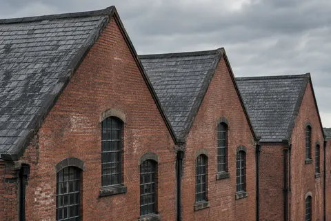 Three red-brick warehouse gables with weathered slate roofs and narrow dark windows viewed obliquely.