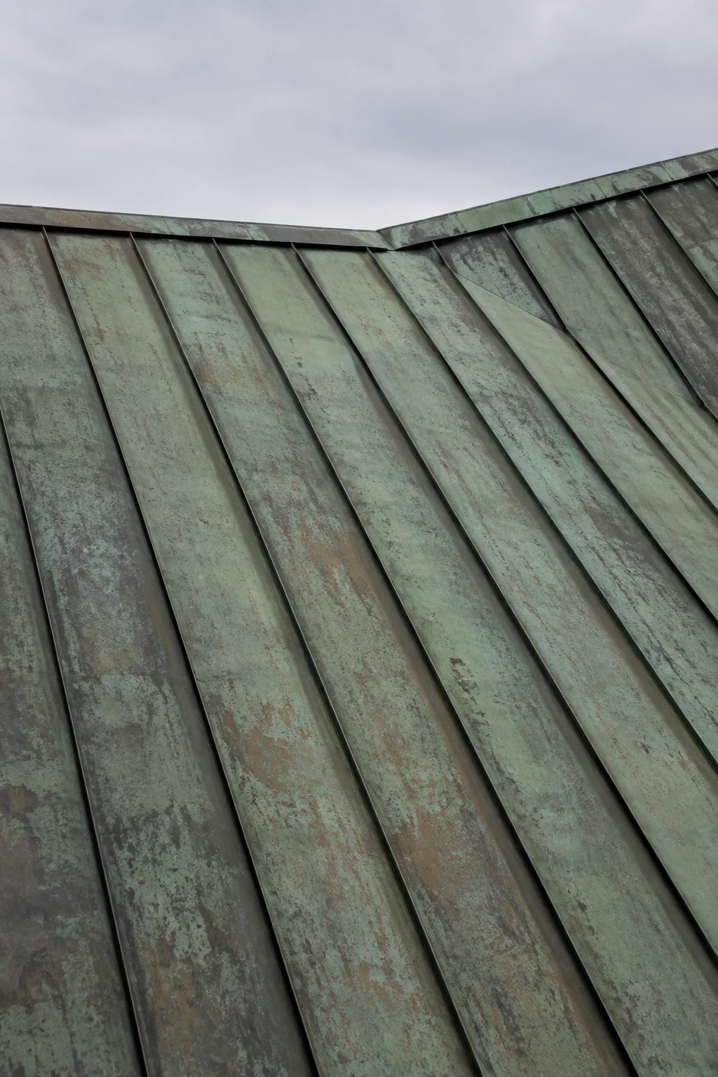 A close copper roof with green and brown weathering, standing seams and a shallow change of roof plane.