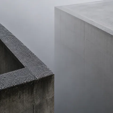 A dark wet concrete parapet corner in the foreground and a pale blank roof mass across dense gray fog.