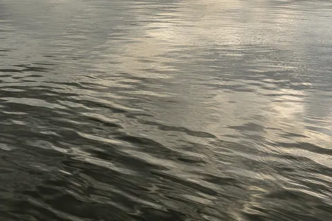 Fine silver-gray ripples cross quiet water, with a darker diagonal band in the lower left and pale reflected light above.