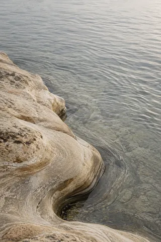 A pale weathered stone shelf curves into clear silver-gray tidal water.
